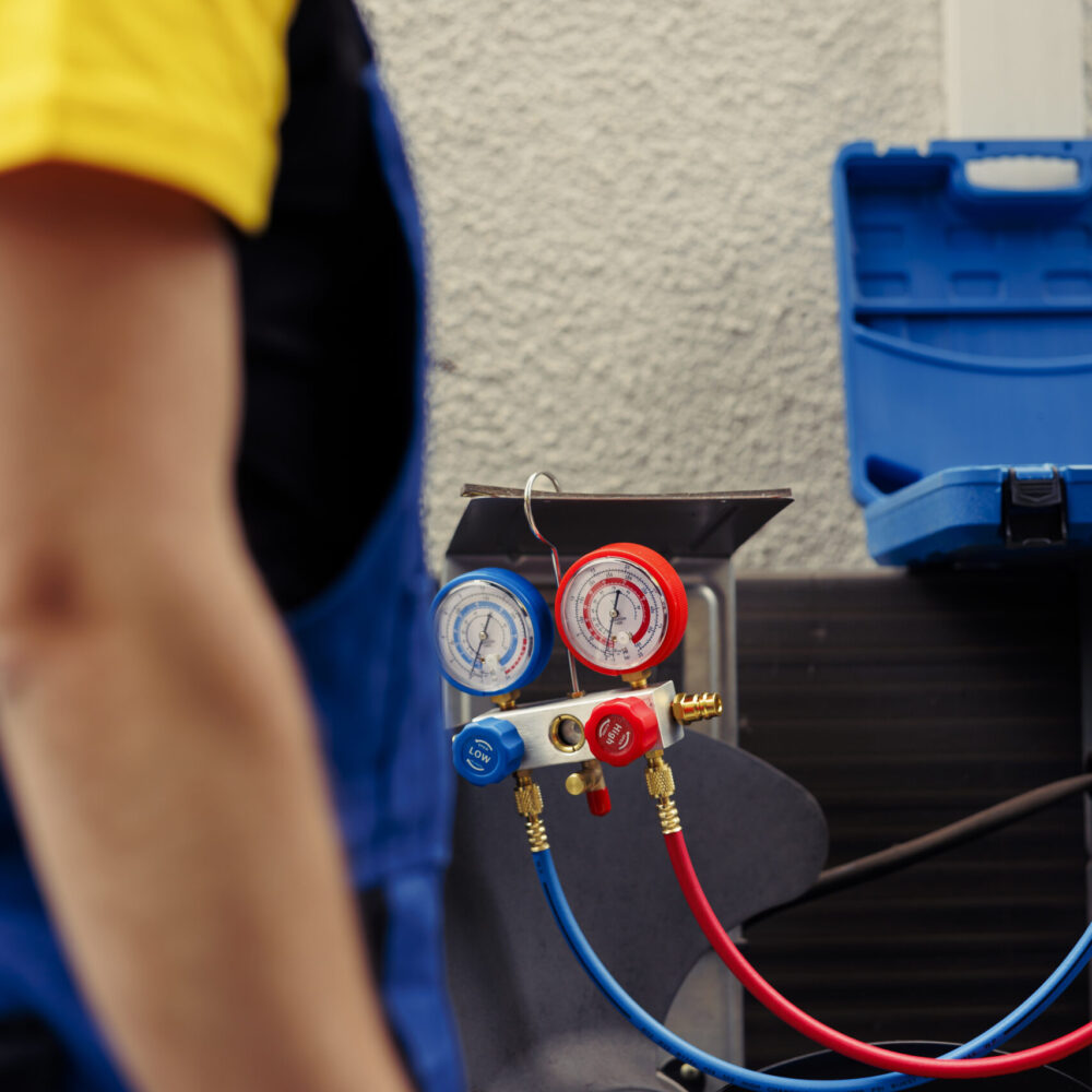 Adept repairman hired to check outdoor hvac system refrigerant tank in need of maintenance, using manometers. Licensed serviceman with ac gauges vacuum pump looking at air conditioner freon levels