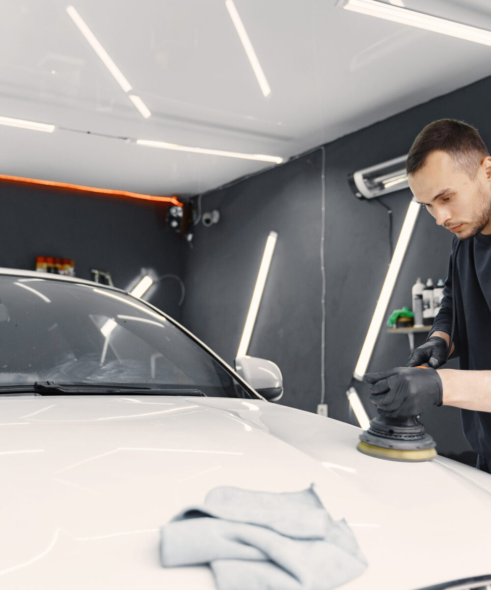 Man in a garage. Worker polish a car. Man in a black uniform.